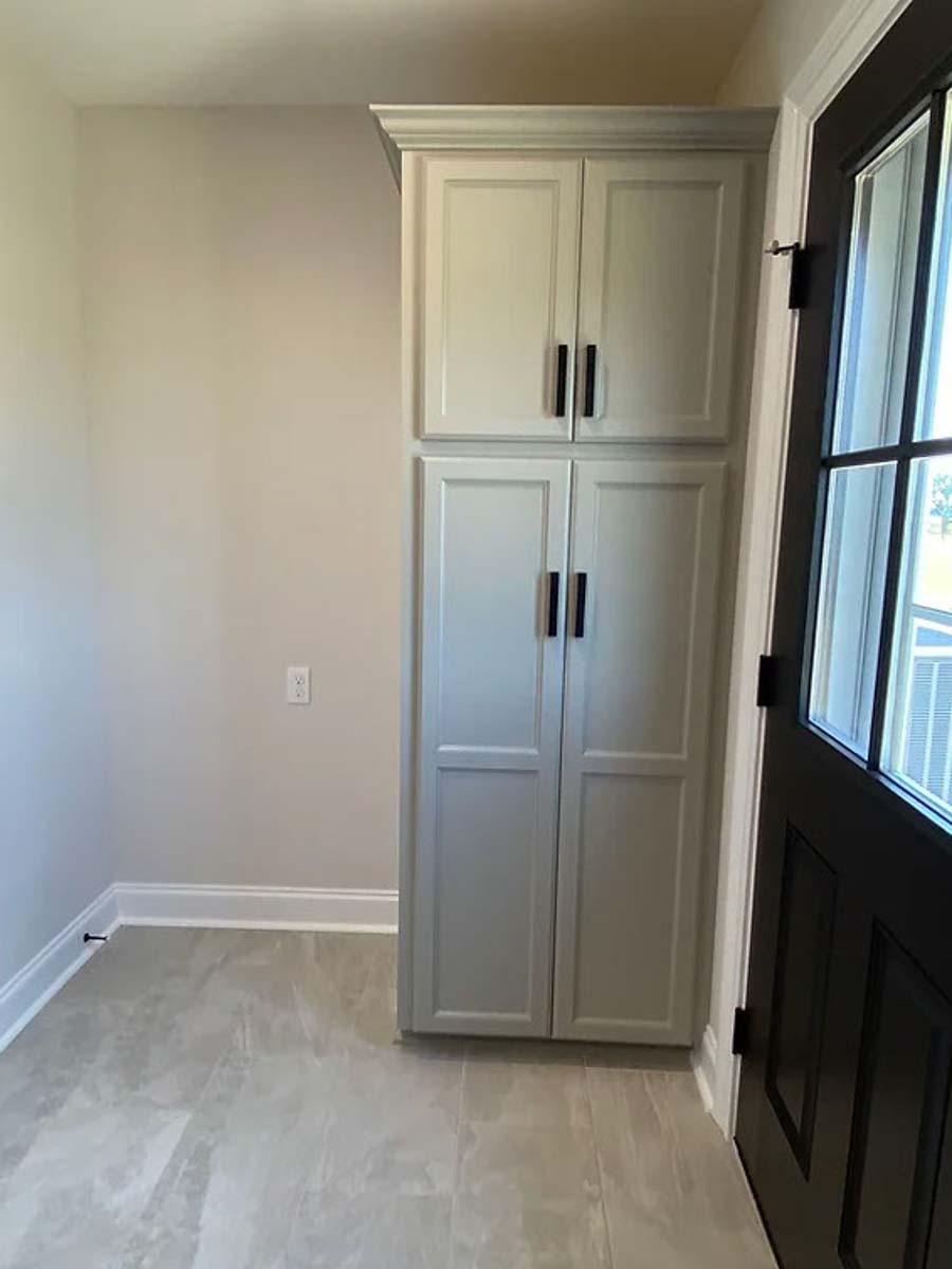 Tall pantry cabinet with panel doors and crown molding, adjacent to a black paneled door with a sidelight window.