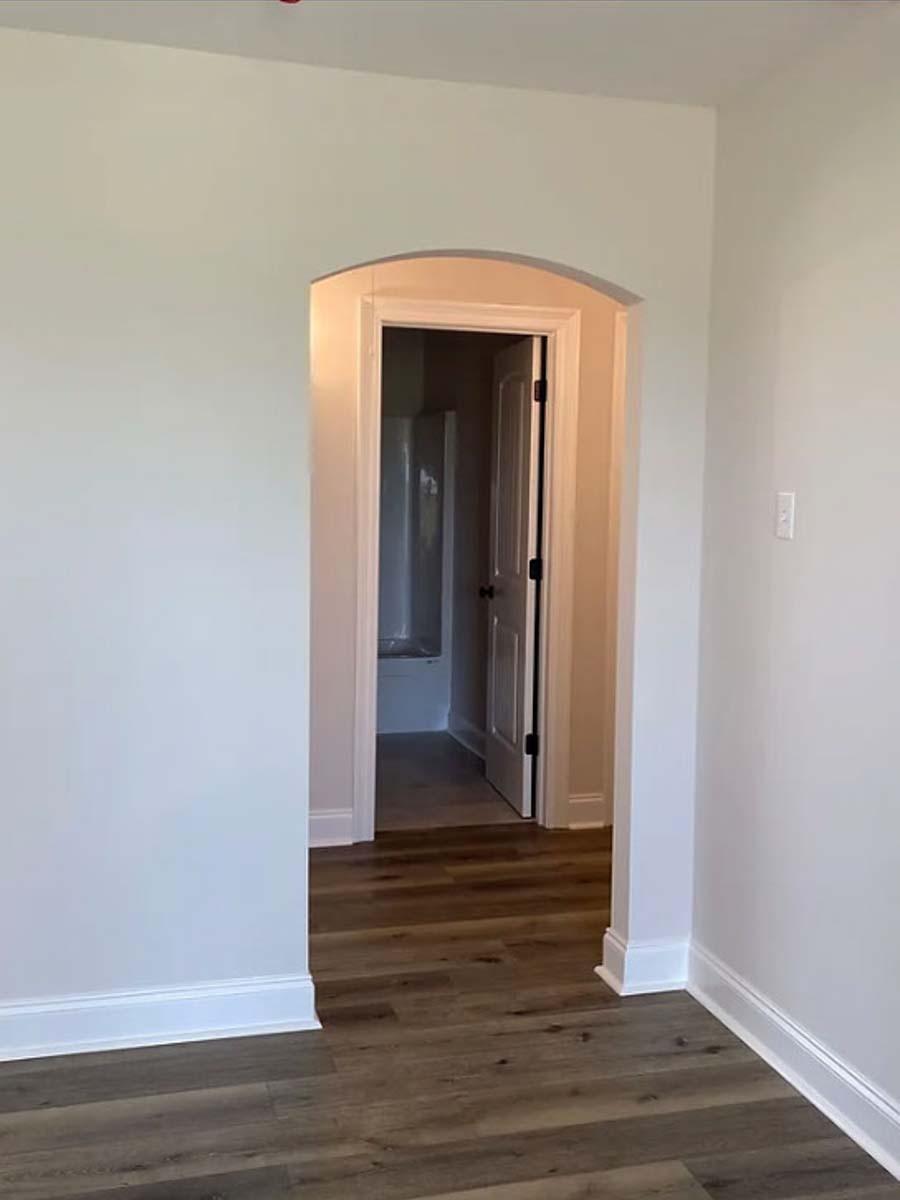 Interior view of a hallway with an arched doorway leading to a bathroom with a tub and an open door.