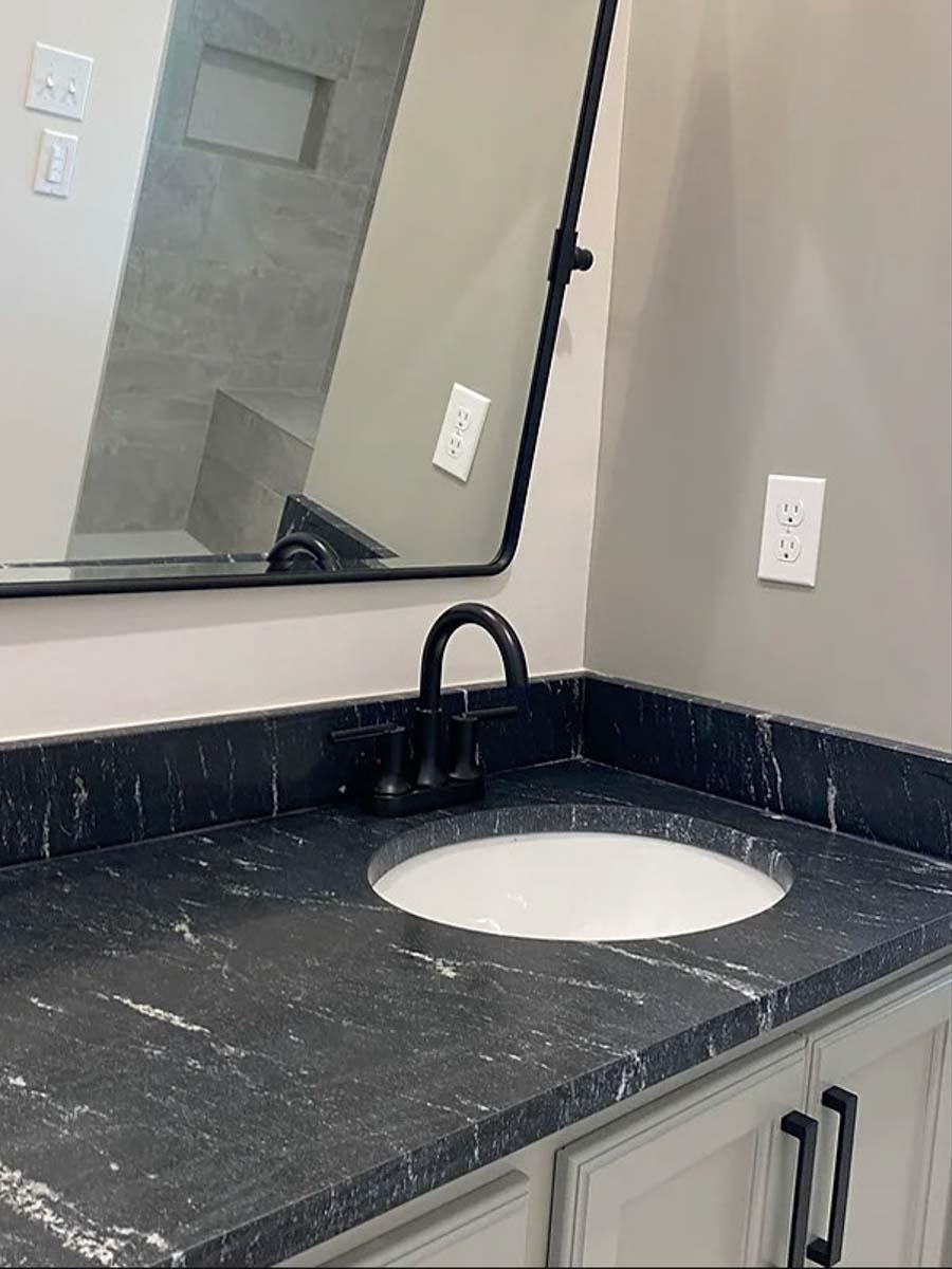 Bathroom vanity with black granite countertop, white undermount sink, matte black faucet, and light gray cabinetry.