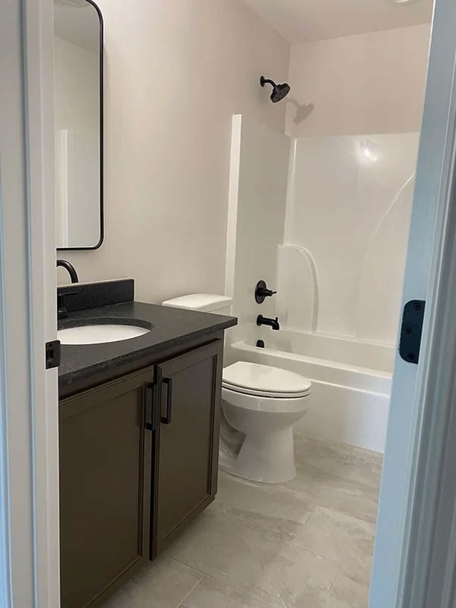 Bathroom with single vanity, toilet, and bathtub with shower. Tall, rectangular mirror above vanity.
