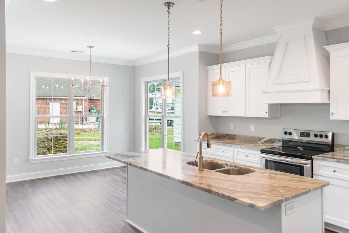 Kitchen featuring a large island with sink, white cabinetry, stainless steel range, and a dining area with large windows.