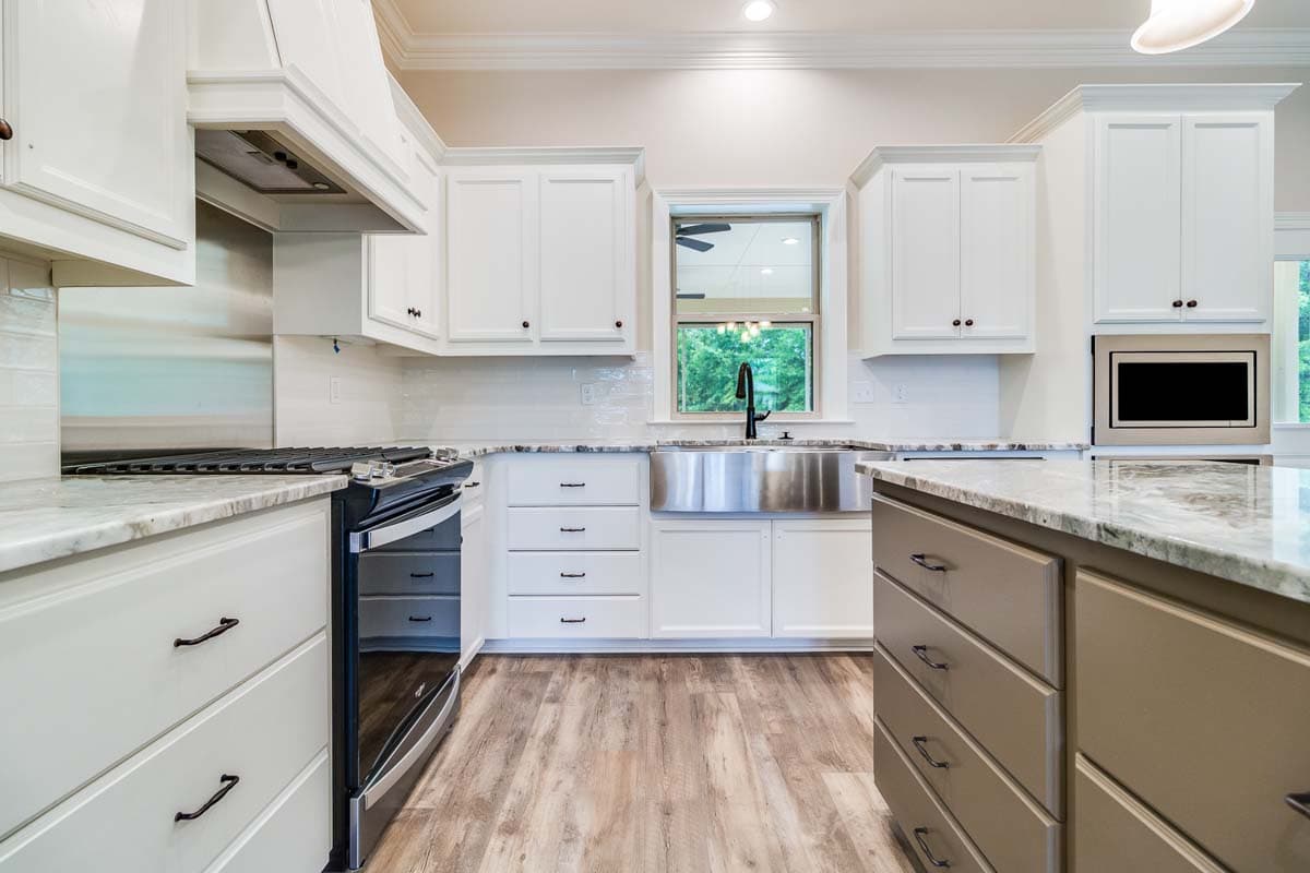 Interior view of a kitchen featuring white shaker cabinets, stainless steel farmhouse sink, gas range, and granite countertops.