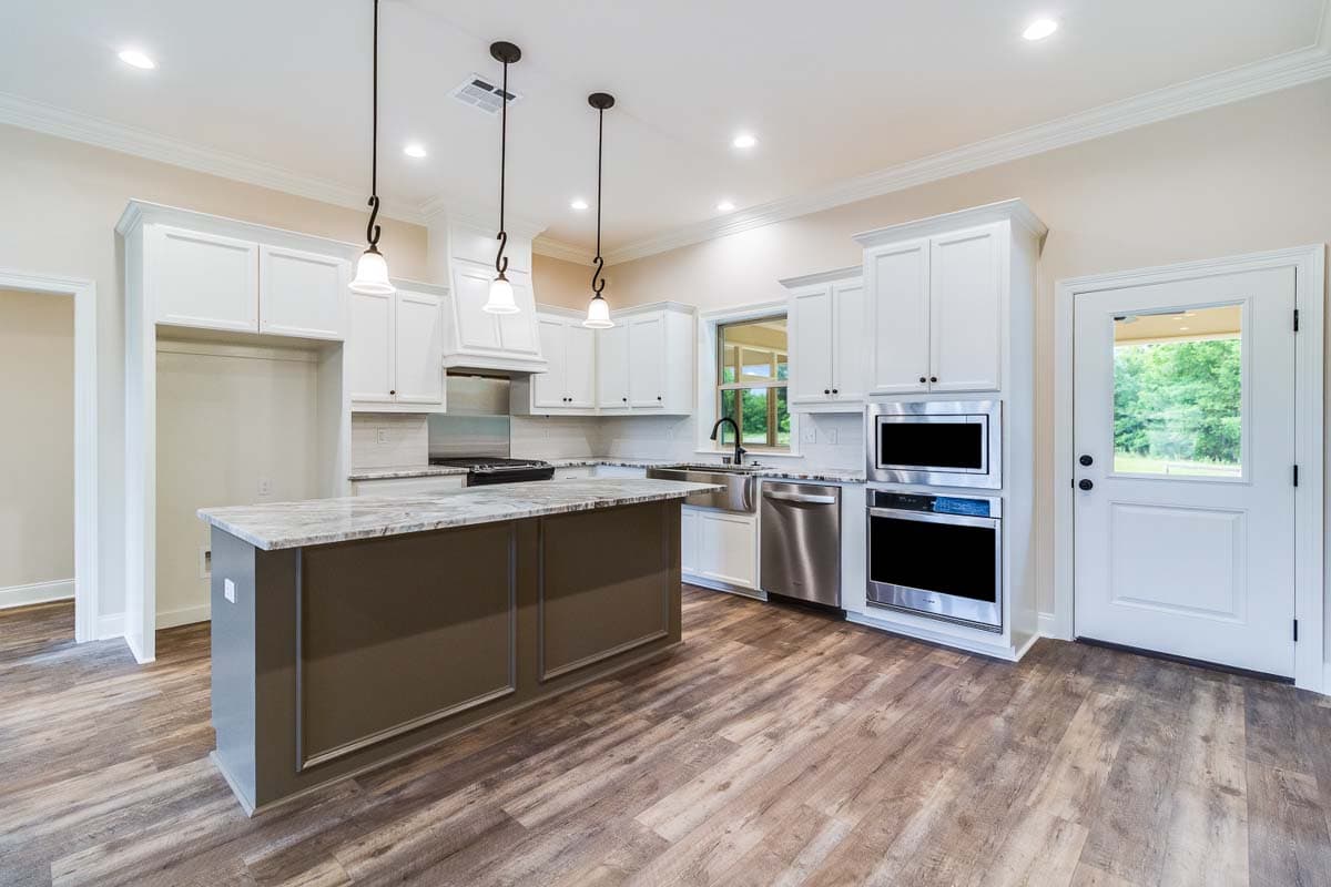 Kitchen with white cabinets, large island with granite countertop, stainless steel appliances, and wood-look flooring.
