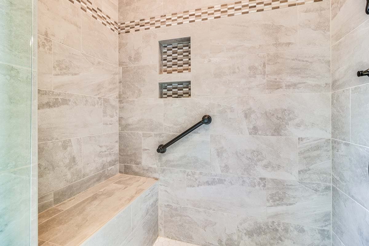 Shower interior with large format stone-look tile, tiled bench, recessed niches with mosaic tile, and grab bar.