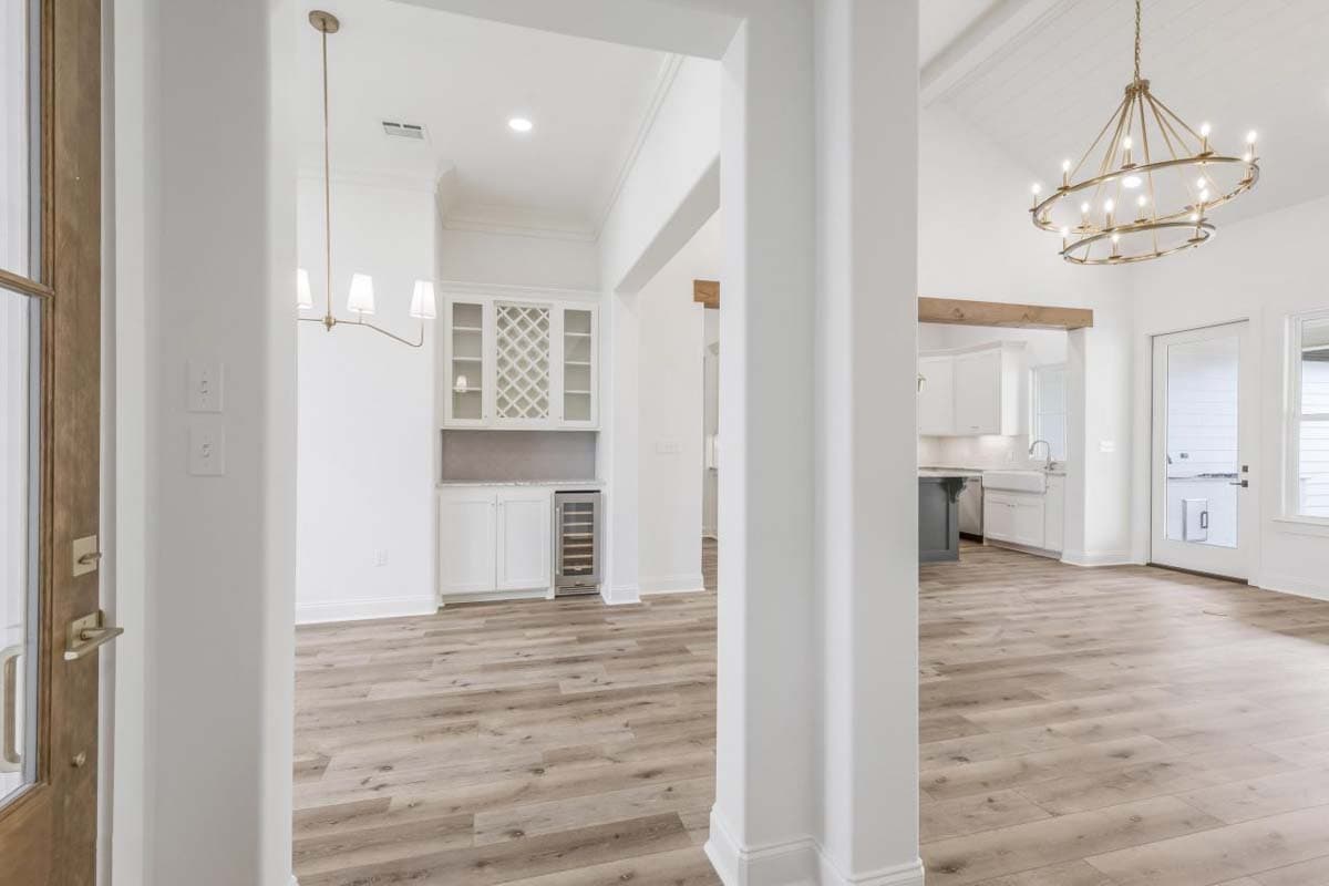 Interior view of a house with a wet bar, kitchen, and dining area with wood beam ceiling and large chandelier.