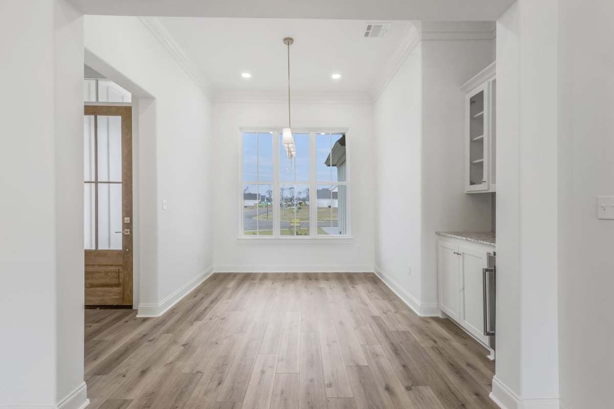 Interior view of an empty room with wood-look flooring, a large window, a built-in cabinet, and a glass-paneled door.