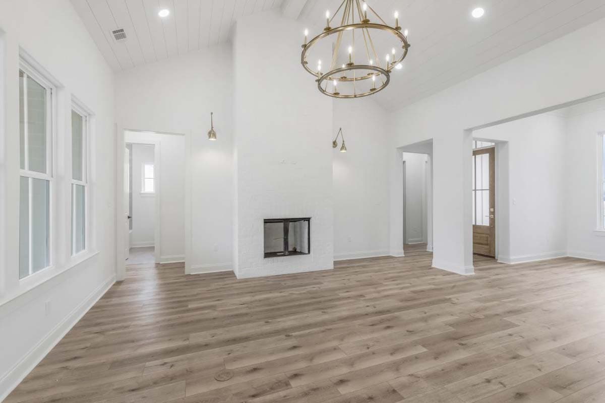 Interior view of a great room with vaulted ceiling, fireplace, and large windows. A chandelier hangs from the ceiling.
