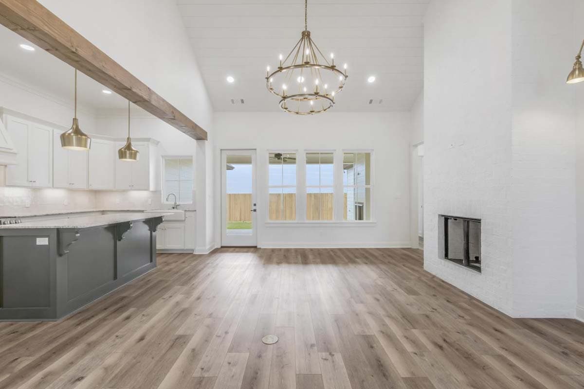 Interior view of open-concept living space with vaulted ceiling, wood beam, kitchen island, and brick fireplace.