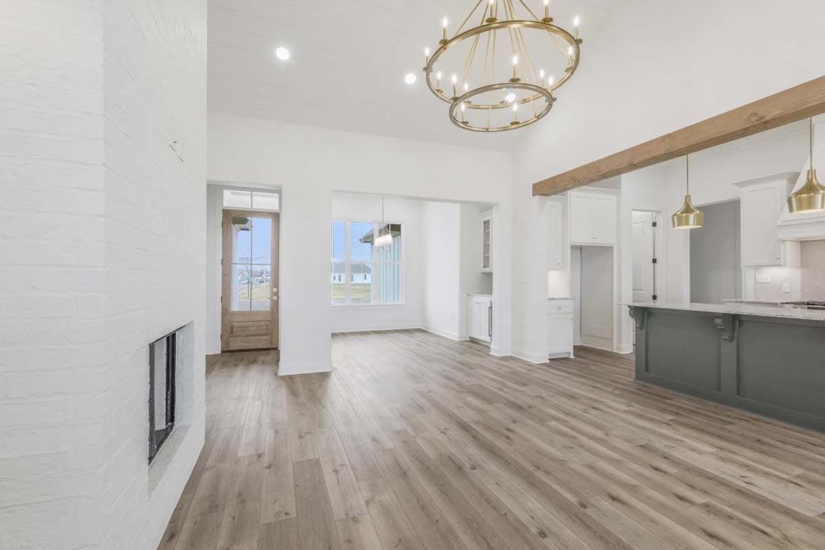 Open concept living area with vaulted ceiling, white brick fireplace, island kitchen, and wood beam accents.