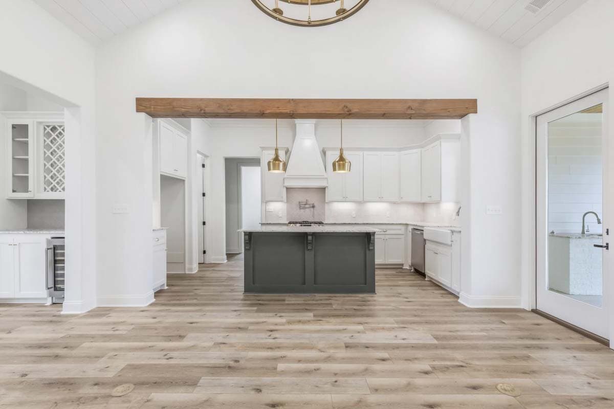 Interior rendering of a spacious kitchen with white cabinets, a large gray island, vaulted beamed ceiling, and wood-look flooring.