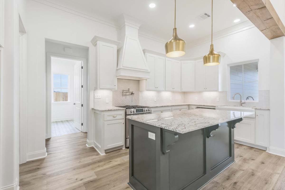 Kitchen with white cabinets, granite island, range hood, pendant lights, and farmhouse sink.