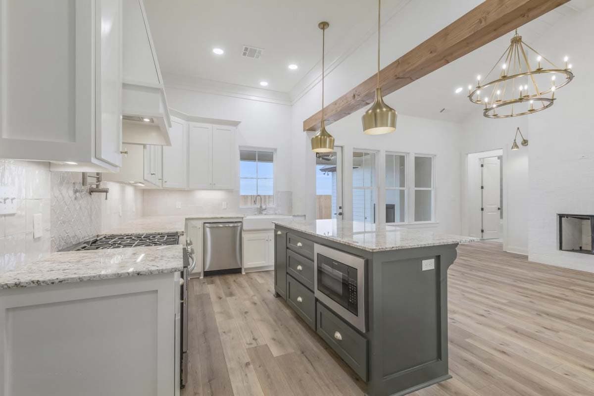 Kitchen with white cabinets, island with microwave, stainless steel appliances, and wood beam ceiling.