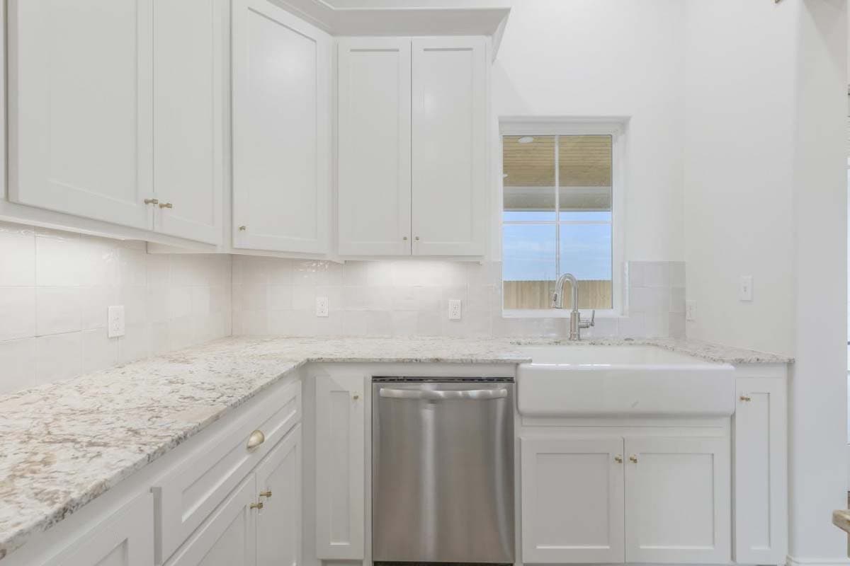 Kitchen featuring white cabinetry, granite countertops, apron sink, stainless steel dishwasher, and a large window.
