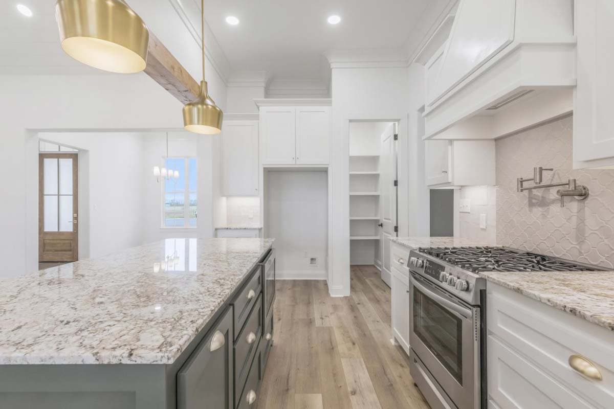 Kitchen with large island, granite countertops, stainless steel gas range, and walk-in pantry with shelves.