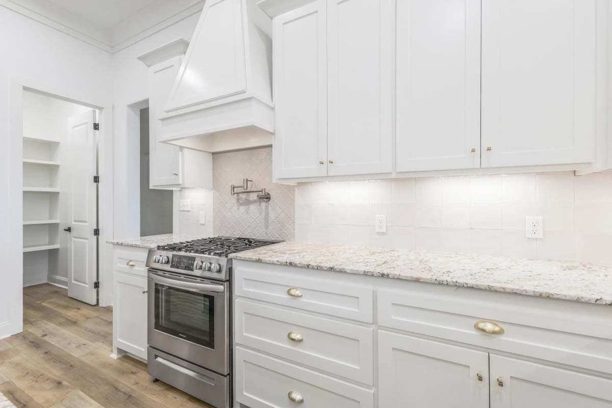 Kitchen featuring white cabinets, granite countertops, stainless steel range, pot filler, and pantry access.