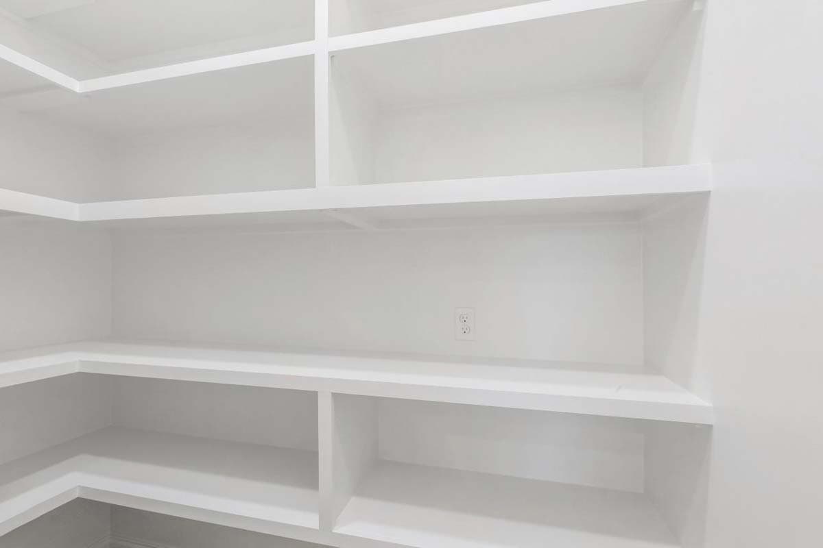 Corner pantry with white built-in shelves and a single electrical outlet.