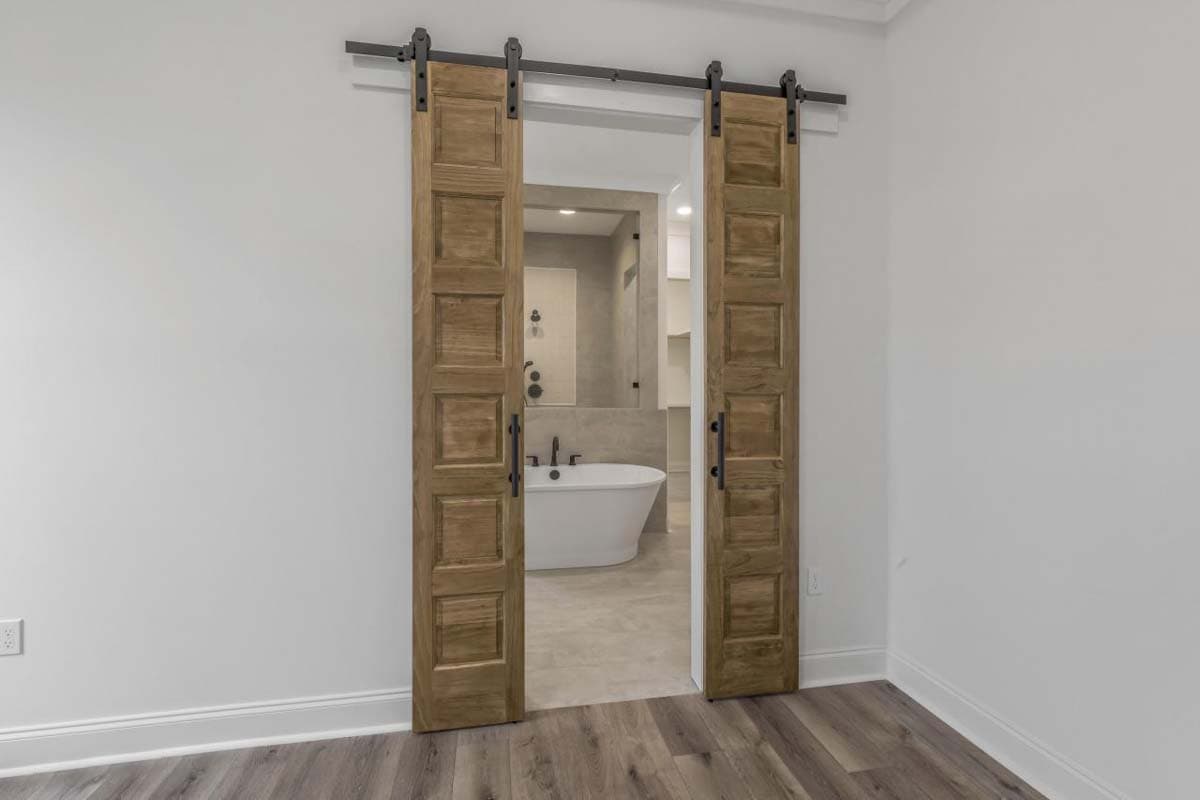 Two wooden sliding barn doors open to a bathroom with a freestanding tub and walk-in shower.