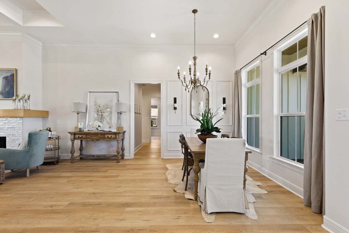 Dining room with wood floor, chandelier, wainscoting, and large windows. View of hallway and living room with fireplace.