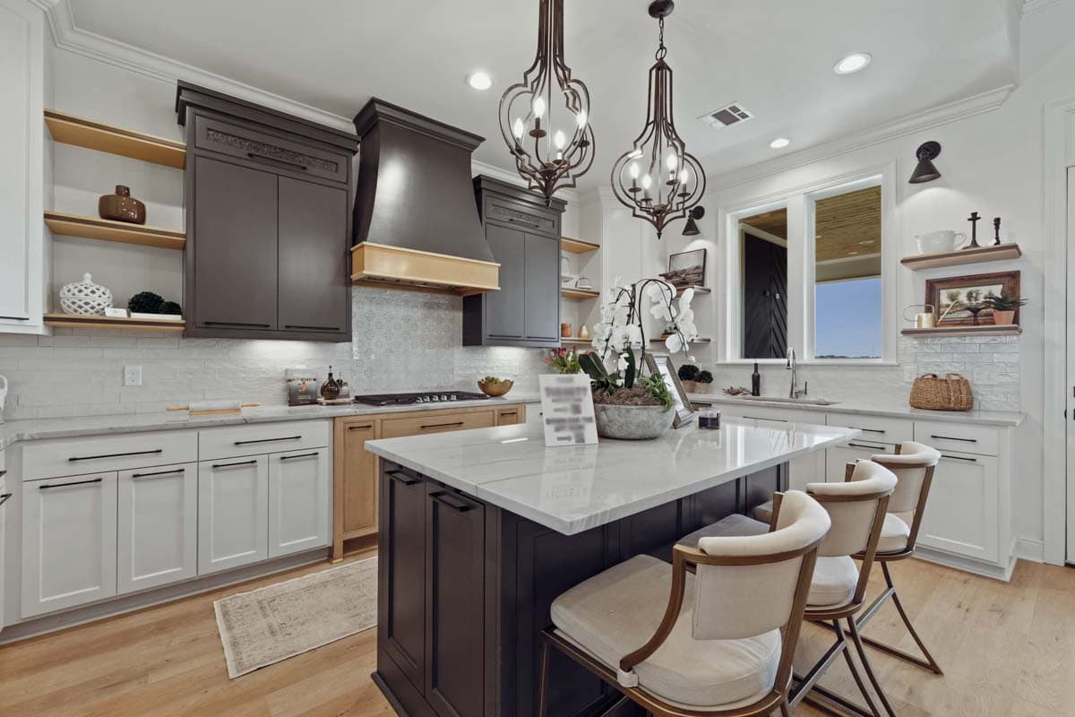 Kitchen featuring a dark island with marble countertop, two-tone cabinets, subway tile backsplash, and decorative pendant lights.