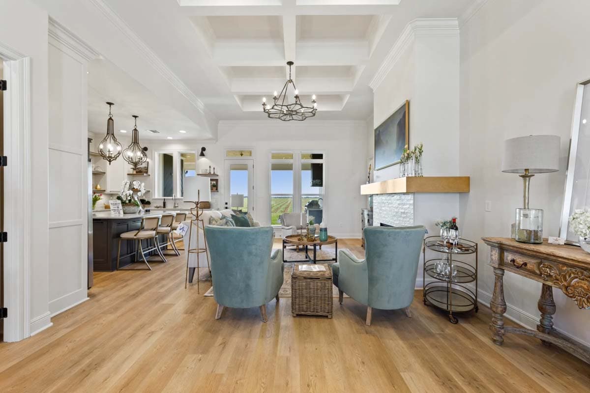 Open concept living area with coffered ceiling, fireplace, kitchen island with bar seating, and large windows.