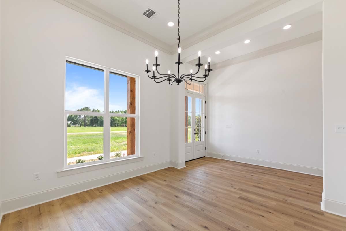 Interior view of a room with a large window, double doors, hardwood floors, and a chandelier.