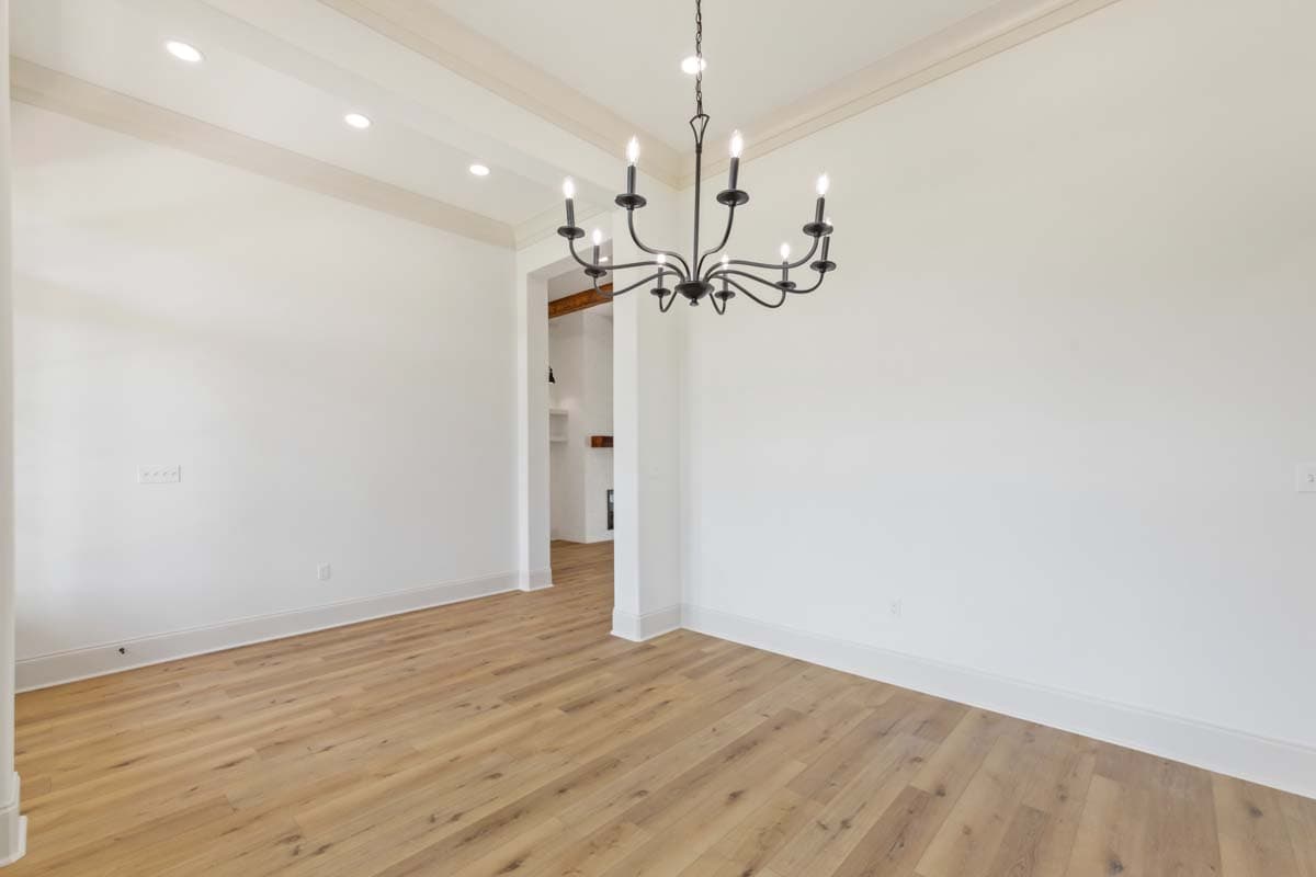 Interior view of a room with a black chandelier, coffered ceiling, and wood plank flooring leading to an archway.