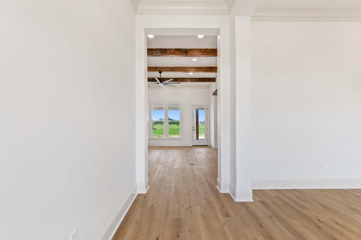Interior view showing a room with rustic wood beams, a ceiling fan, and large windows overlooking a field.