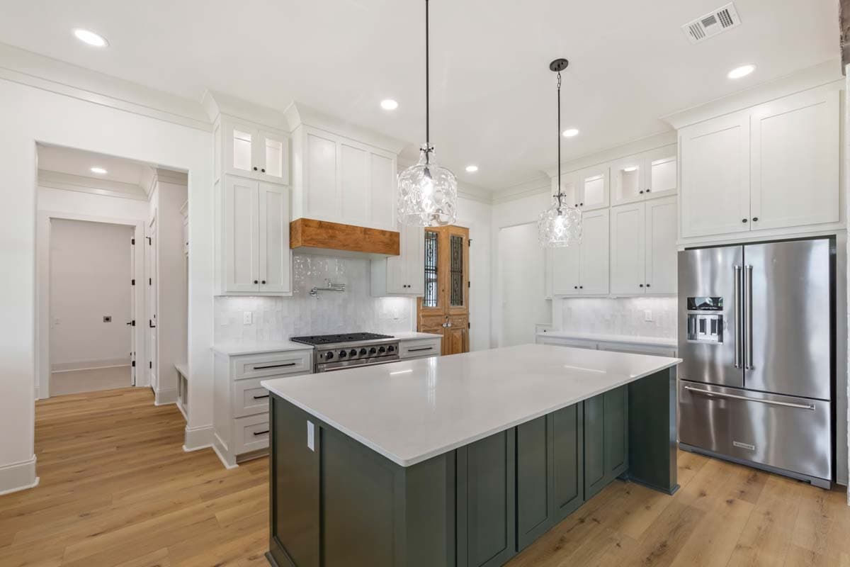 Kitchen with large island, stainless steel appliances, white cabinetry, wood range hood, and wood plank flooring.