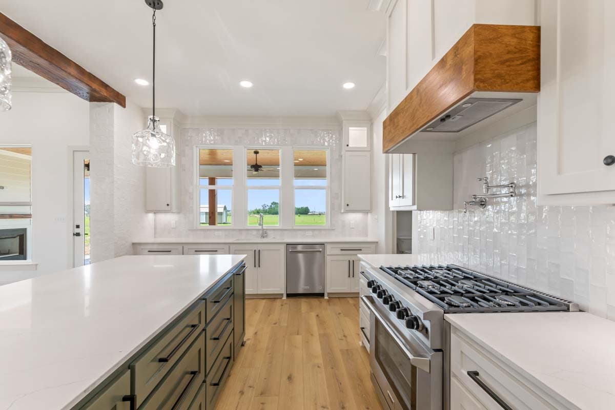 Kitchen with large island, gas range, white subway tile backsplash, and windows overlooking a field.