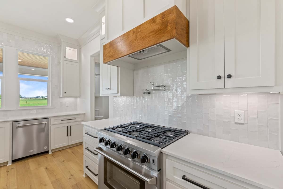 Kitchen with stainless steel range, wood vent hood, white cabinetry, and white tile backsplash.