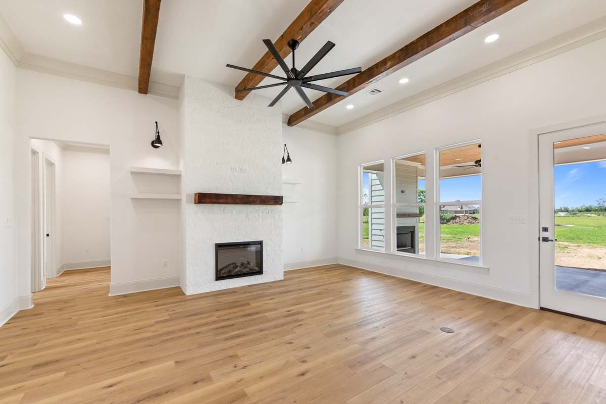 Great room with vaulted ceiling, exposed beams, white brick fireplace, and large windows.