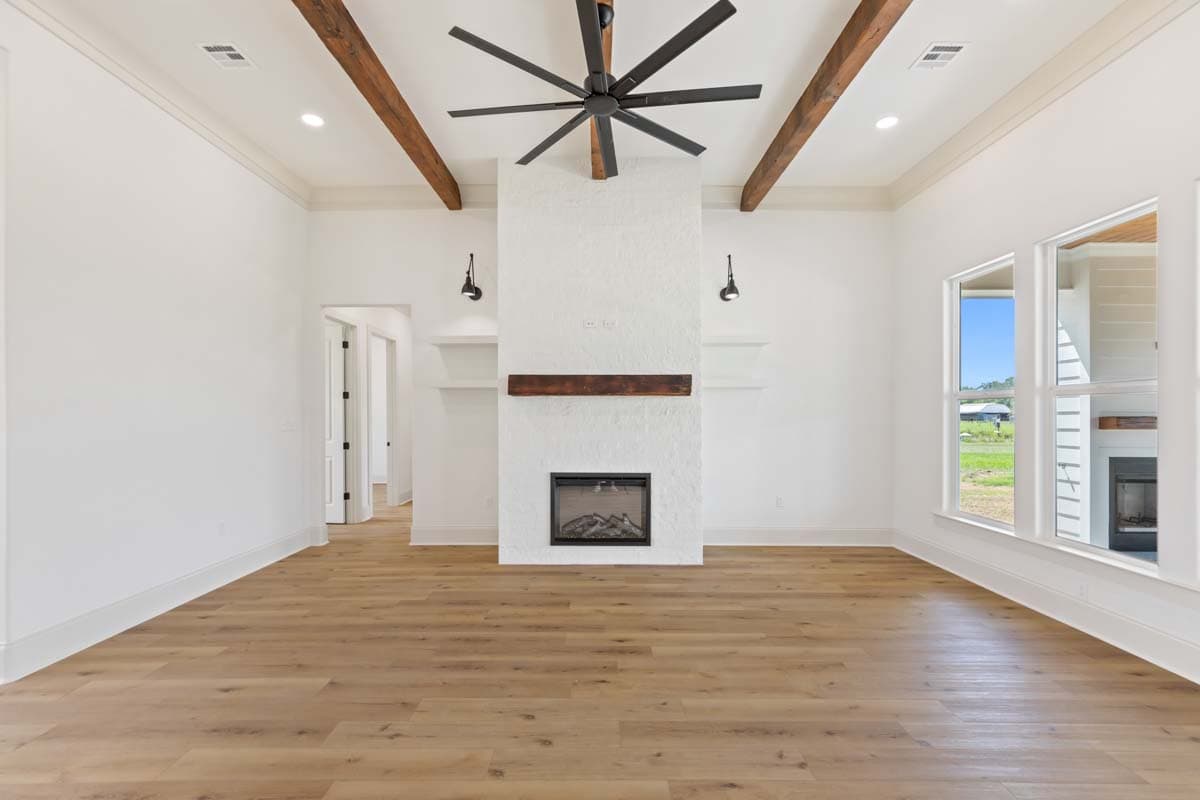 Interior view of living room with vaulted ceiling, exposed wood beams, fireplace, and large windows.
