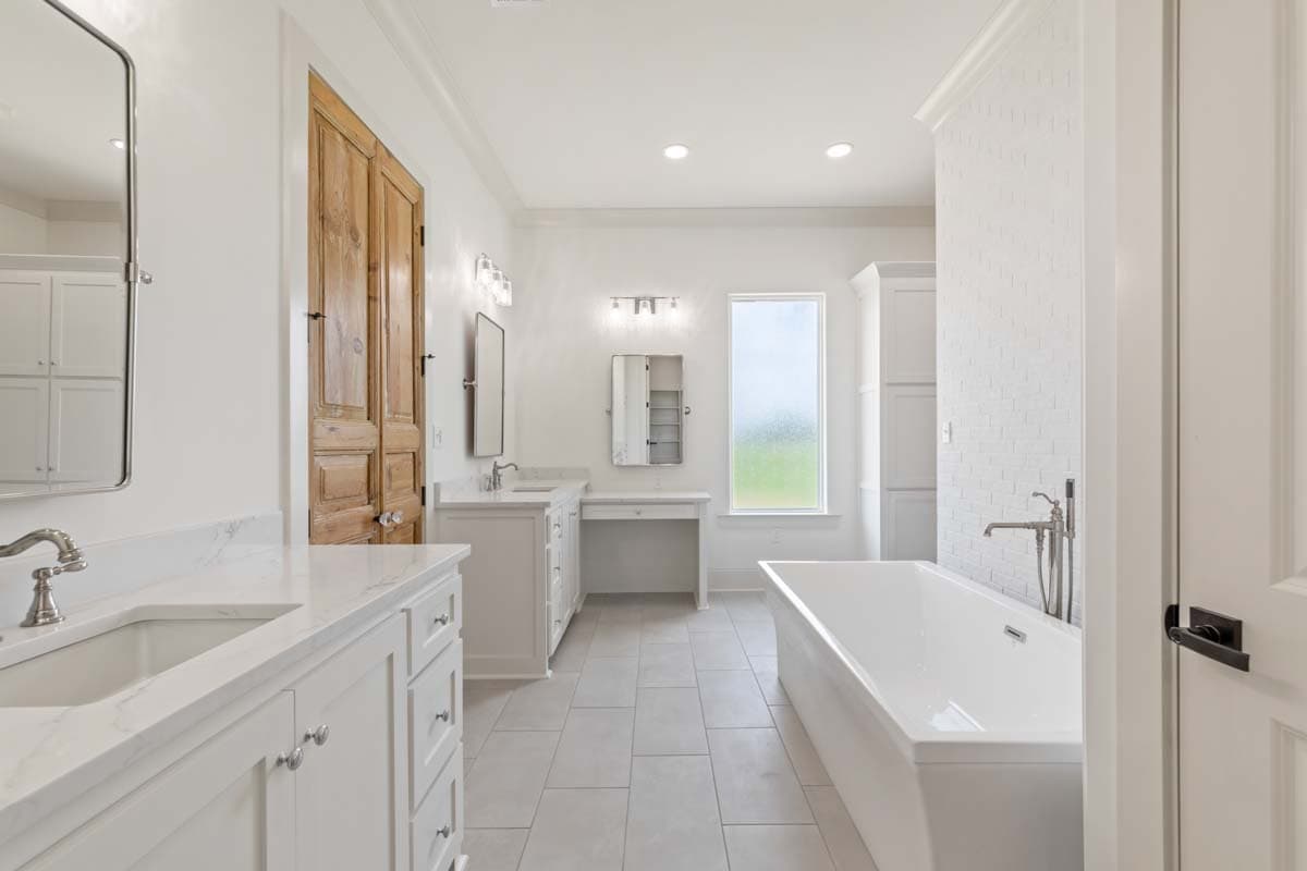 Bathroom with double vanity, freestanding tub, large wood double doors, and a makeup vanity.