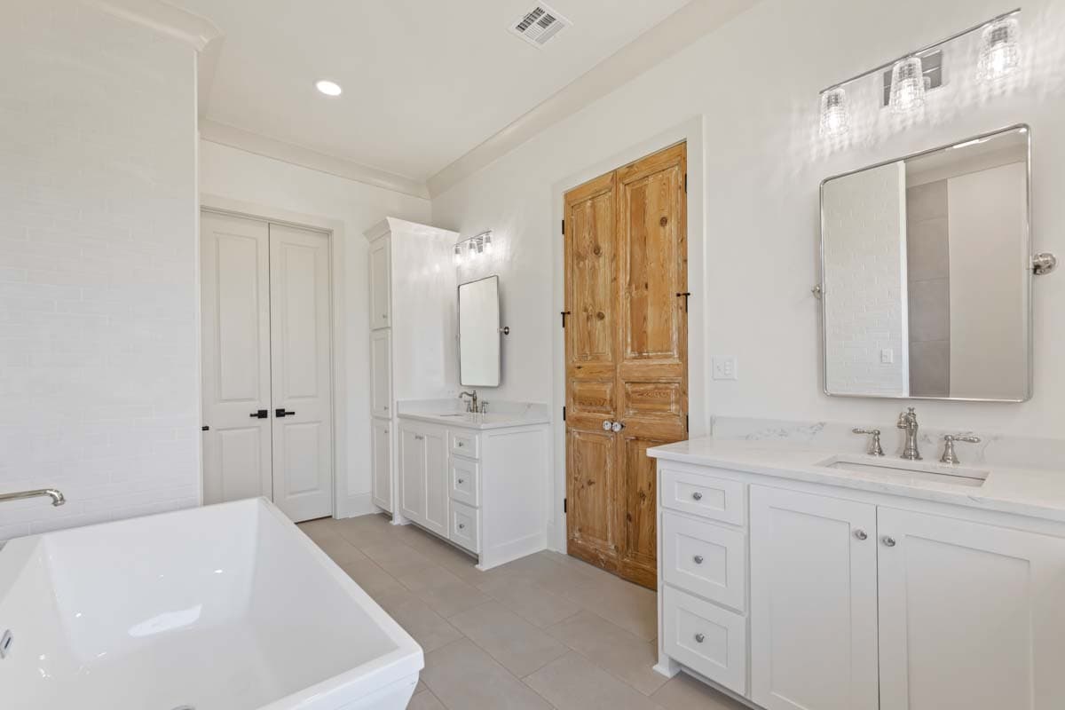 Spacious bathroom with freestanding tub, white dual vanities, and a rustic double wood door.