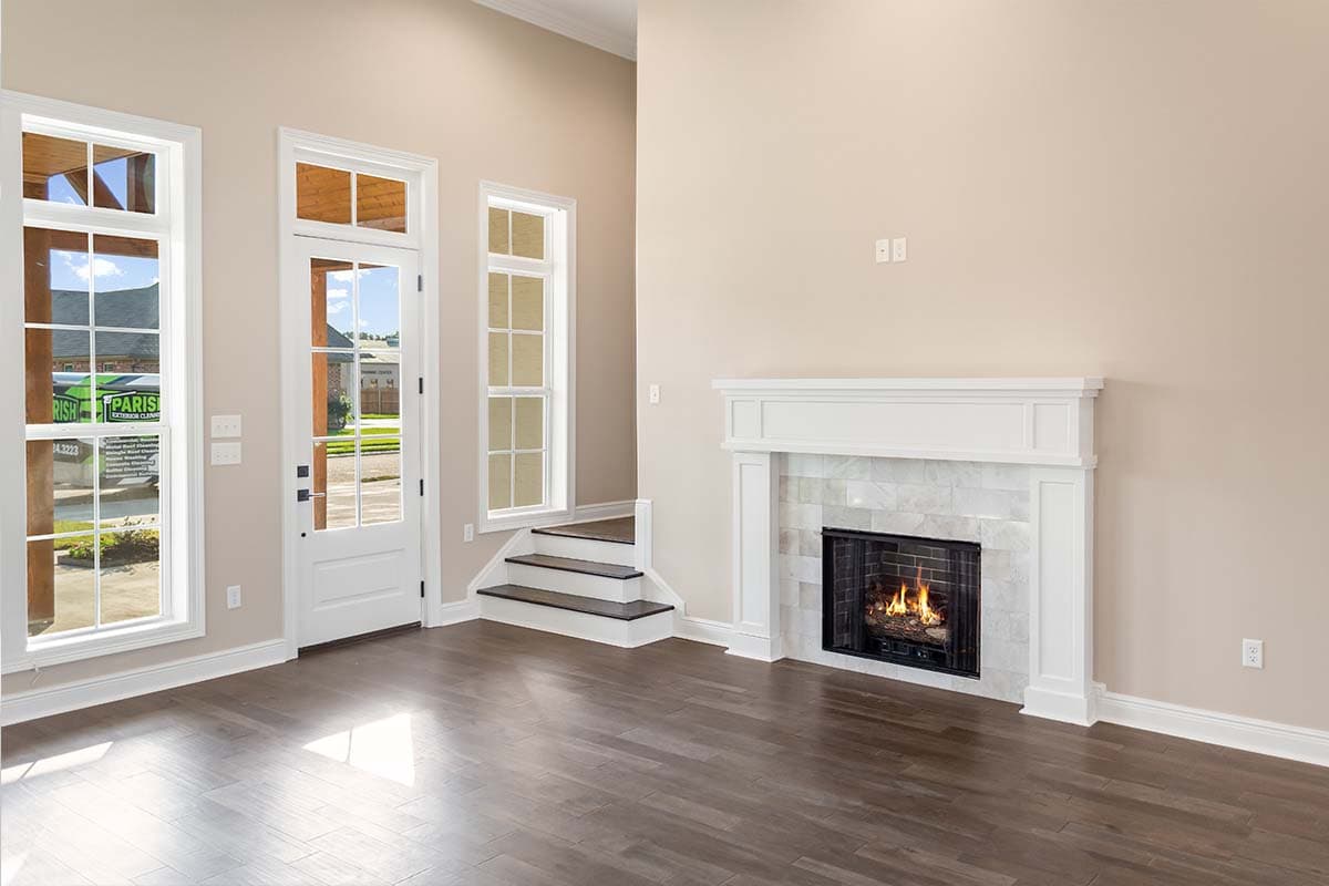 Living room interior with a fireplace, large windows, and a door leading outside. Features vaulted ceilings.