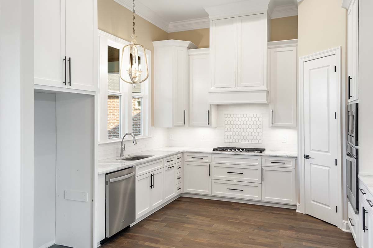 Kitchen interior with white cabinets, stainless steel dishwasher, gas range, and hexagon tile backsplash.