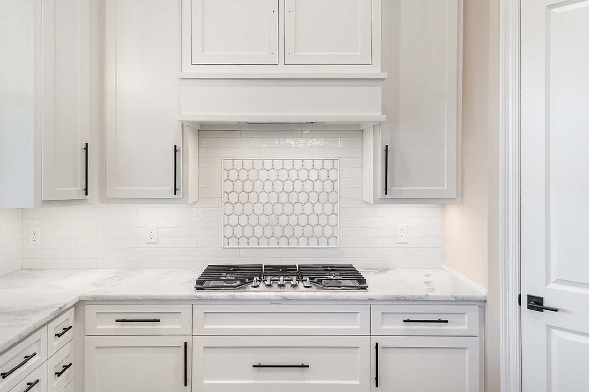 Kitchen counter with gas range, white cabinetry, subway tile backsplash, and honeycomb mosaic accent.