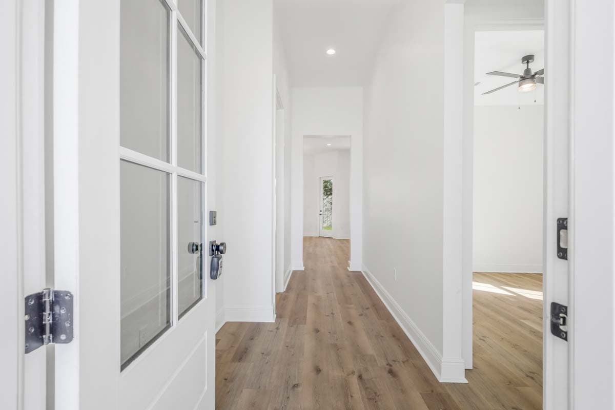 Interior view of a hallway with wood flooring, a glass-paneled door on the left, and openings to rooms.