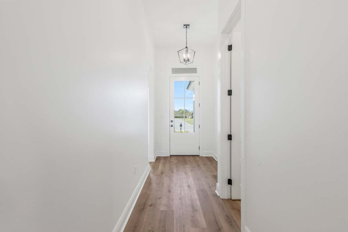 Interior hallway with white walls, wood flooring, and a glass-paneled front door with a geometric lantern.