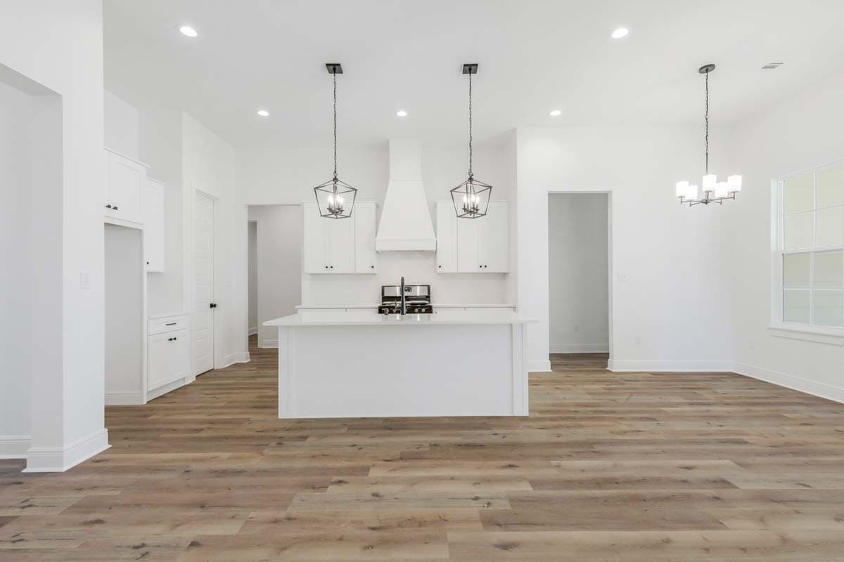 Modern kitchen with white island, range hood, and cabinetry. Open layout with pendant lights.