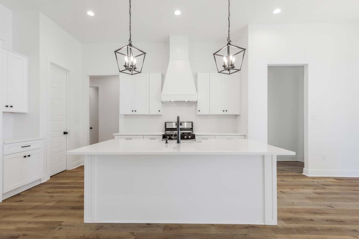 Modern kitchen with white cabinets, large island, range hood, and pendant lights.