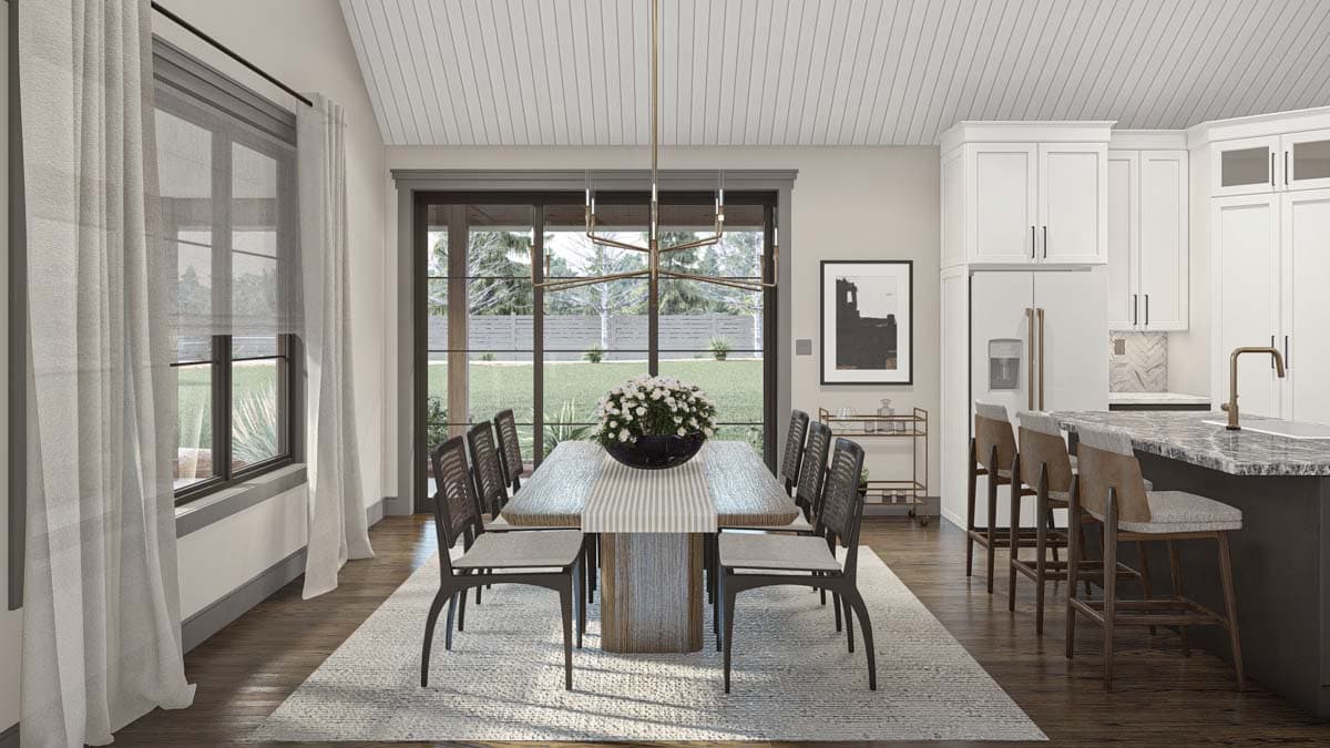 Dining area with rectangular table, eight chairs, and adjacent kitchen island with bar stools, large windows view yard.