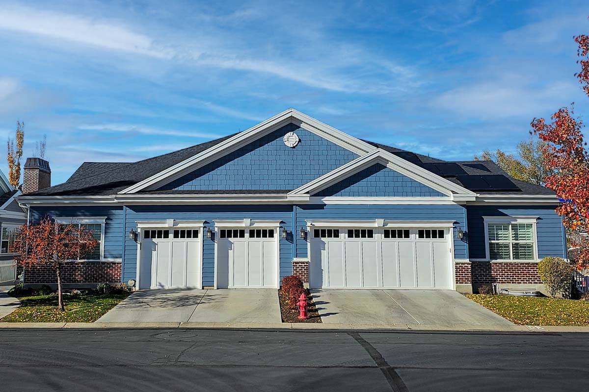 House plan exterior with blue siding, gable roof, and three garage bays. Features include dormers and brick accents on a two-story structure.
