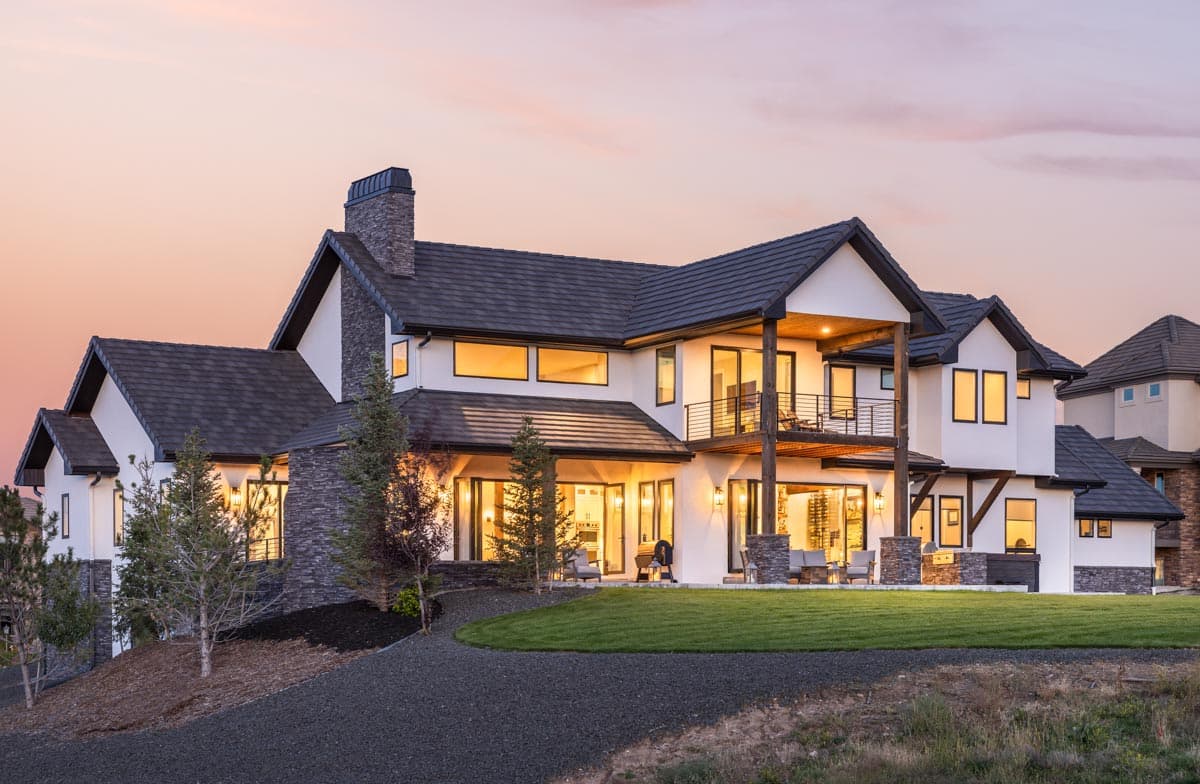 Modern house plan exterior: two stories, stone chimney, upper balcony with railing, and large windows.