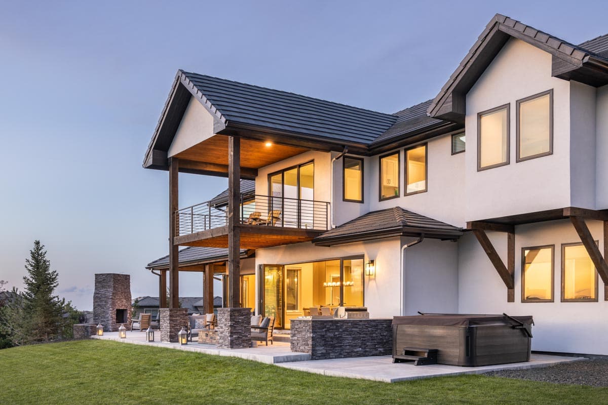 House plan exterior with two-story balconies, stone chimney, hot tub, and multiple gabled rooflines.