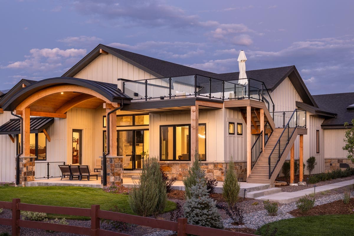 Modern house plan exterior with curved entry, stone accents, large windows, and multi-level deck with glass railings.