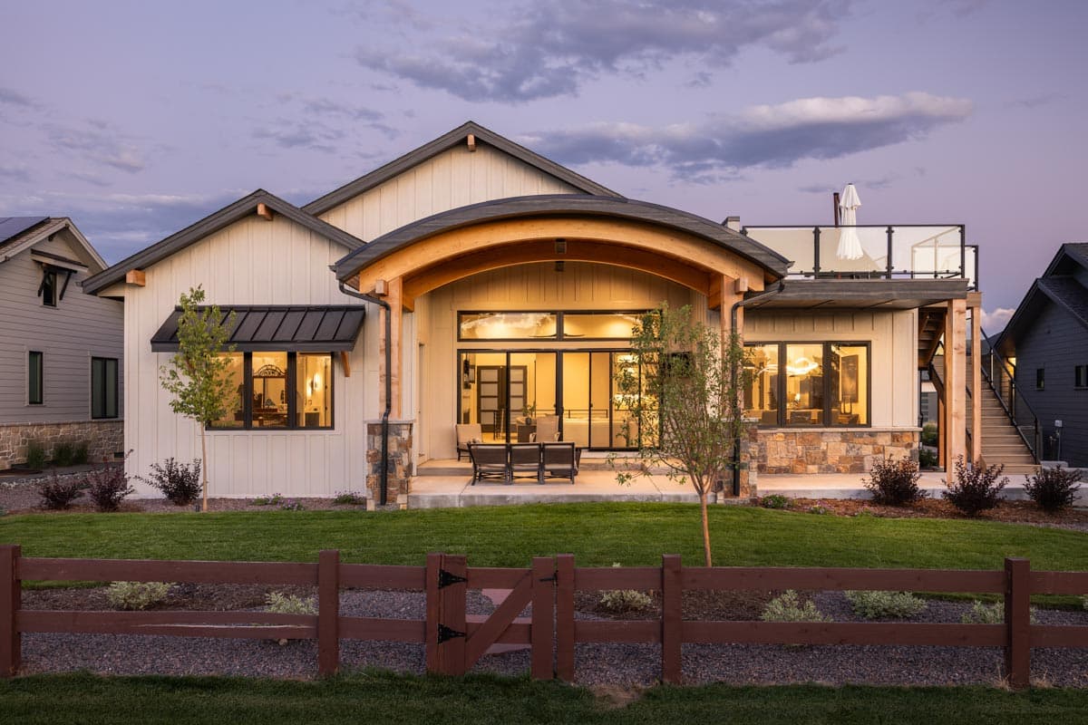 Modern house plan exterior with board and batten siding, stone accents, large windows, and a curved covered patio.