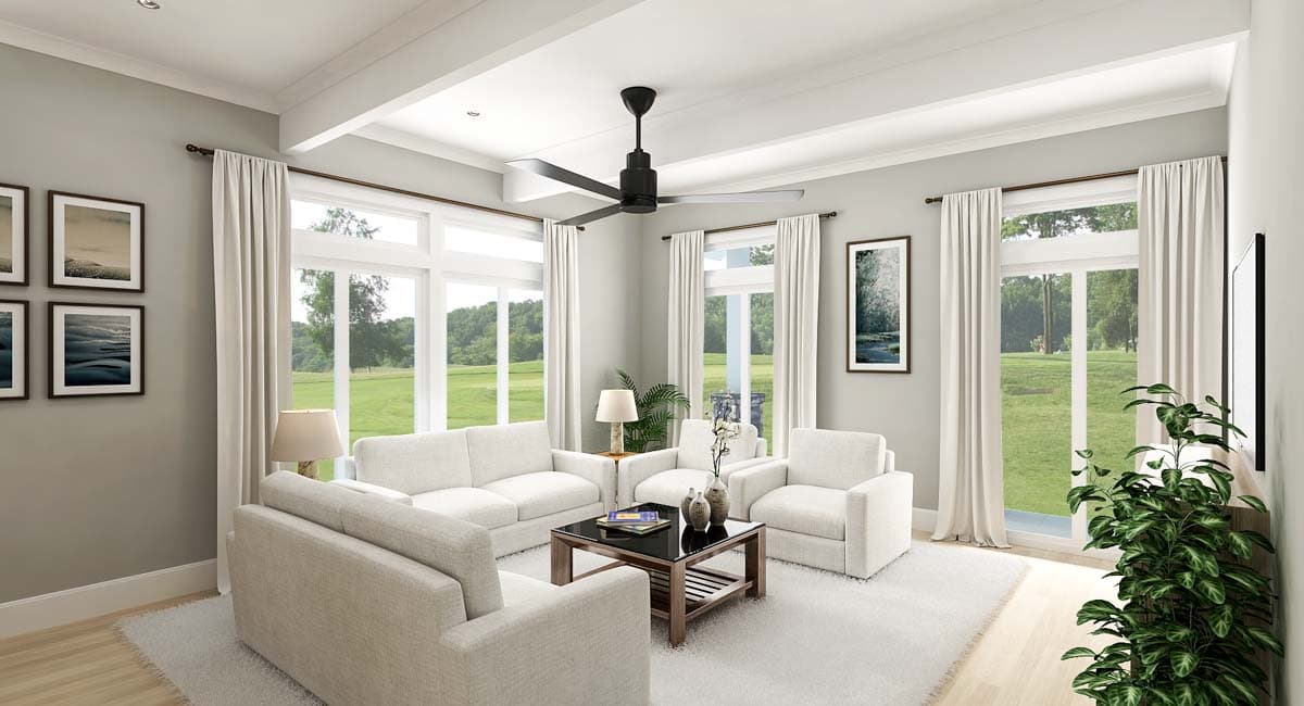 Living room with white sofas, coffee table, ceiling fan, and large windows overlooking a green landscape.