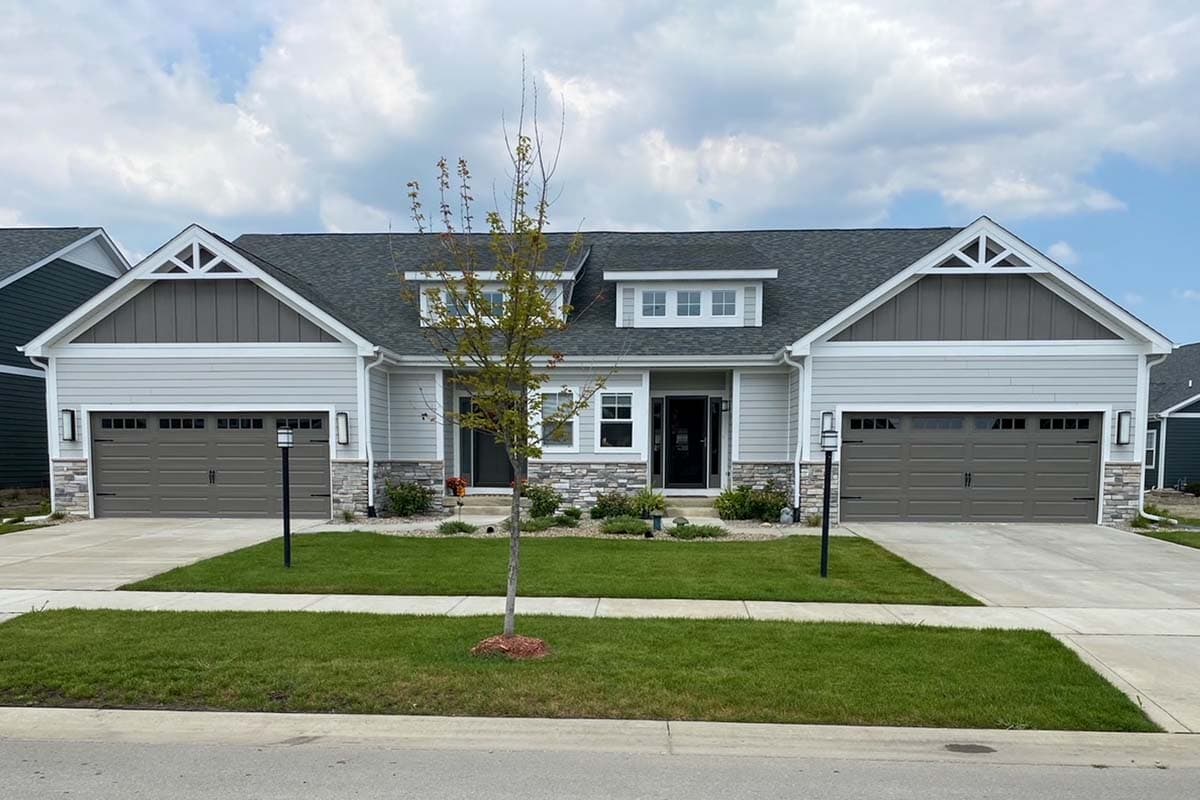 House plan exterior: Modern Farmhouse style, two stories, gable accents, dormers, stone and vinyl siding, and two-car garages.