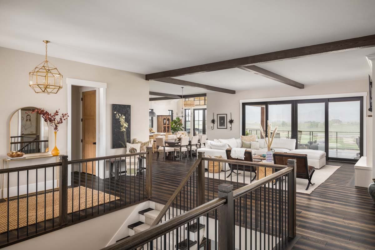 Interior view showing an open living space with exposed wooden beams, a large sectional sofa, dining area, and floor-to-ceiling windows.